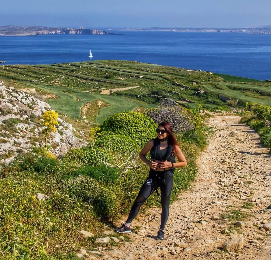 Flor on the Gozo coastal trail — terraced farmland dropping to the sea, Malta visible across the channel, and not another hiker in sight