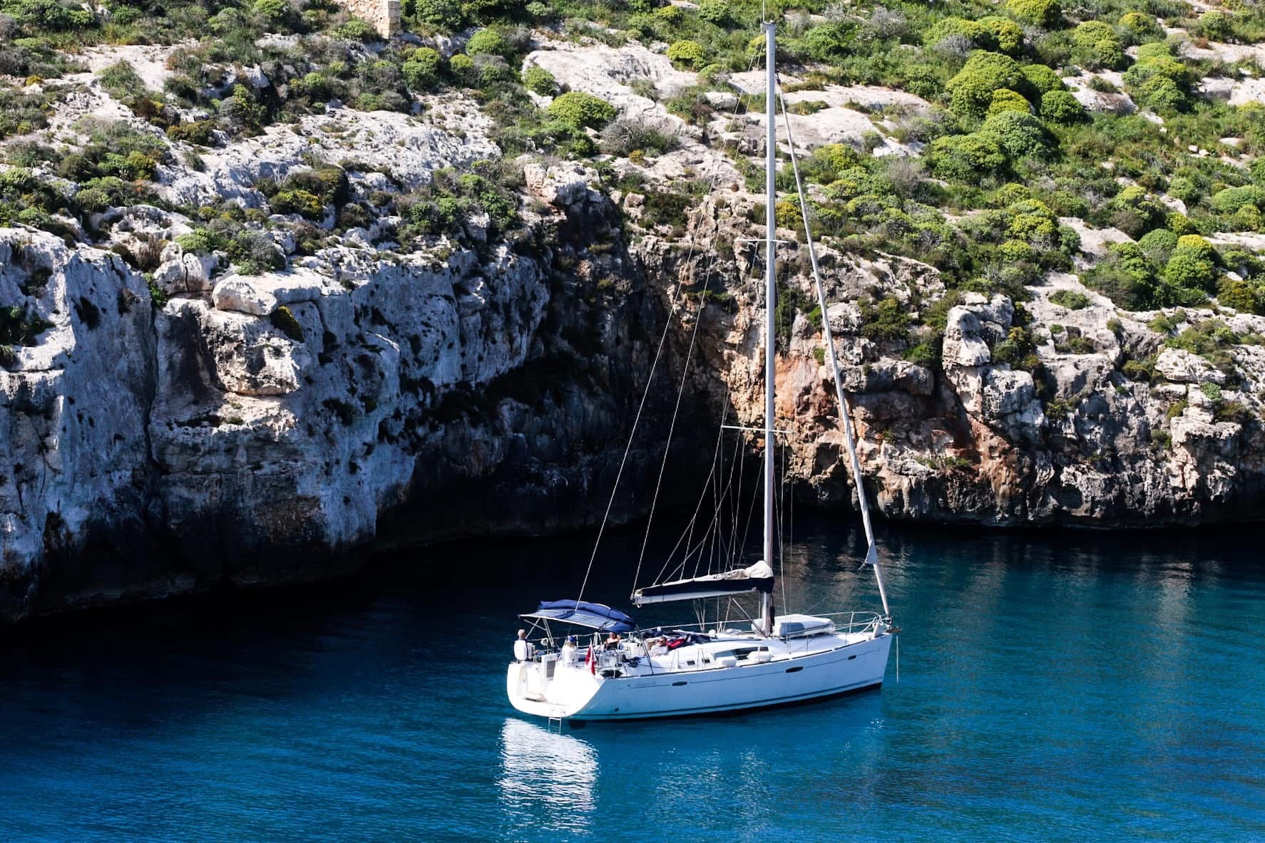 A sailboat anchored in the turquoise waters of Mgarr ix-Xini — limestone cliffs rising on either side, the kind of scene that stops you mid-step
