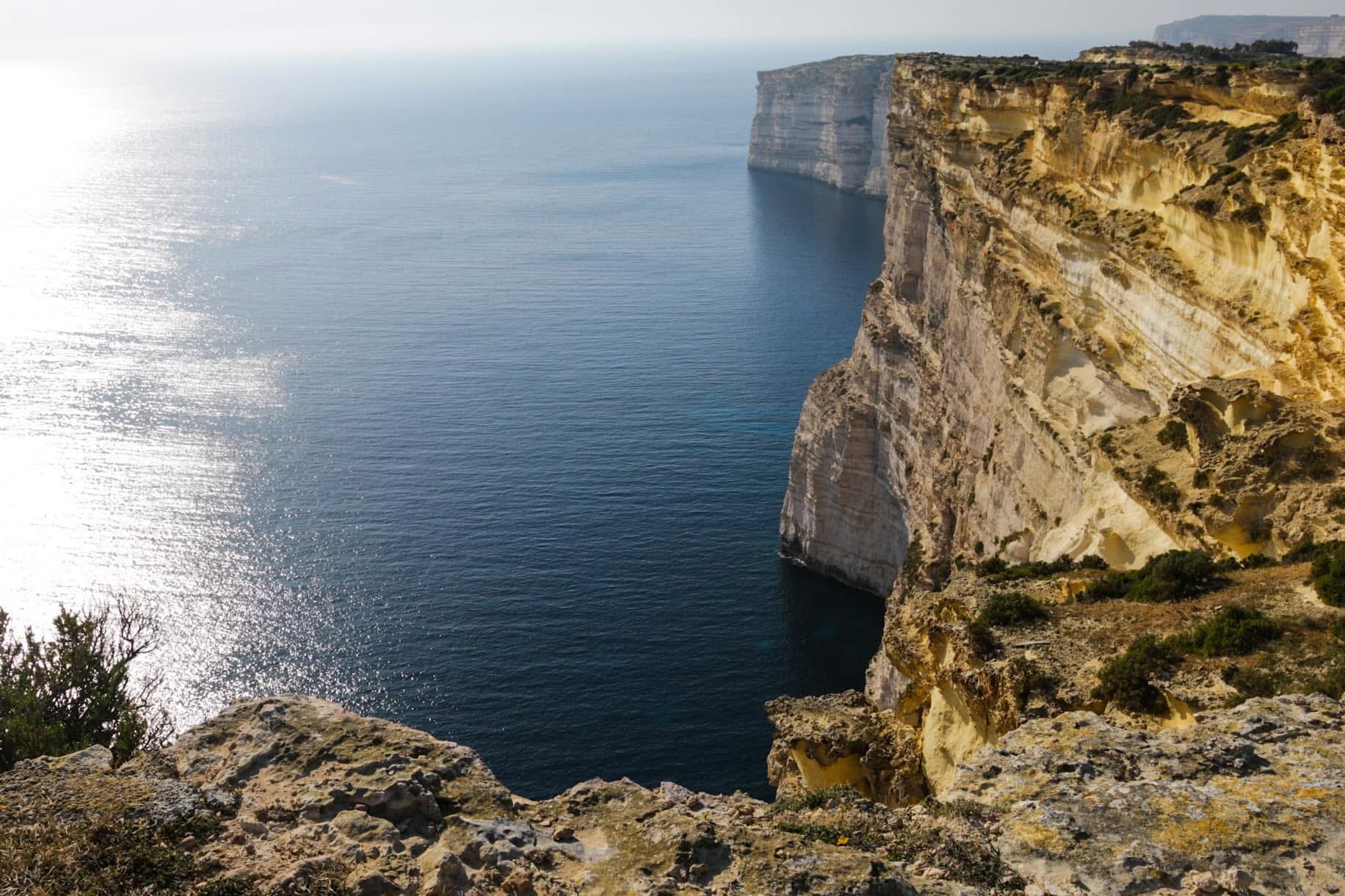 The Sanap Cliffs in late afternoon light — golden limestone walls dropping vertically into deep Mediterranean blue, the kind of view that makes you sit down and just stare